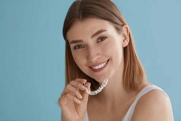 Young woman smiling and holding Invisalign aligners