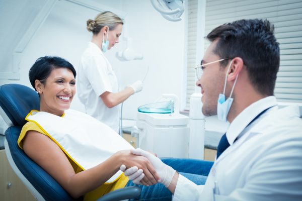 patient in dental chair shaking dentist's hand