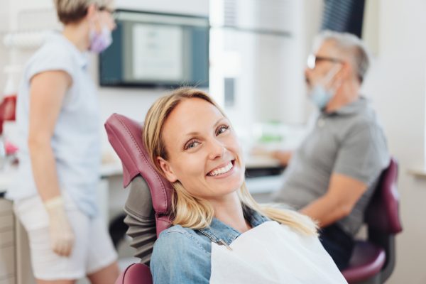 patient smiling in dental chair while dentist speaks to hygienist behind her